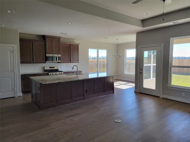 a kitchen with stainless steel appliances granite countertop a stove a sink and a refrigerator with wooden floors