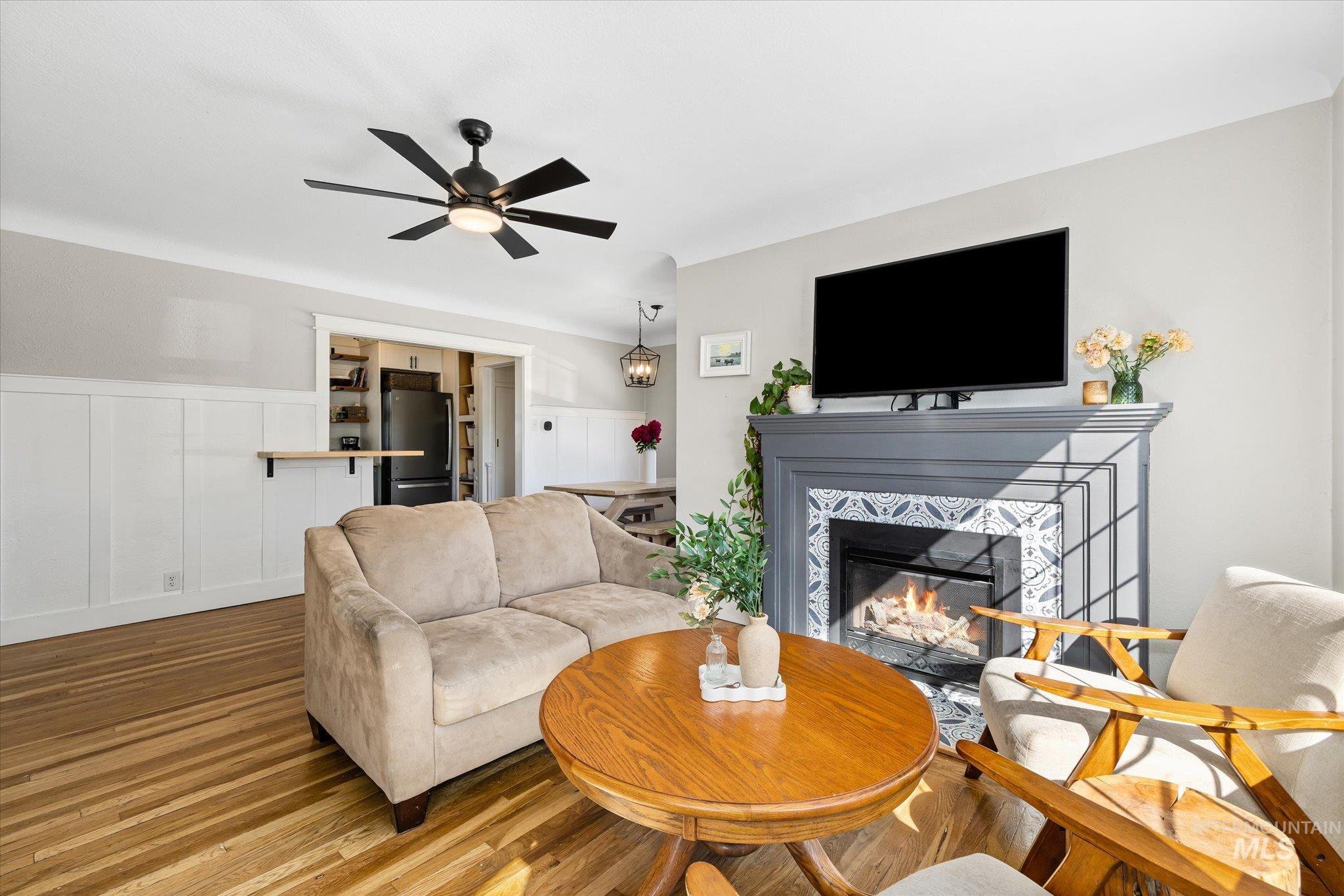 1008 Fillmore Street Caldwell, ID 83605 - Photo 47 of 50 Living room featuring a decorative wall, wood finished floors, a tiled fireplace, a ceiling fan, and wainscoting