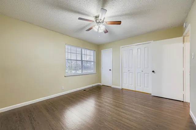 an empty room with wooden floor chandelier fan and windows