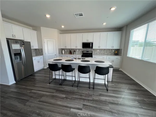 a kitchen with stainless steel appliances a dining table chairs refrigerator and sink