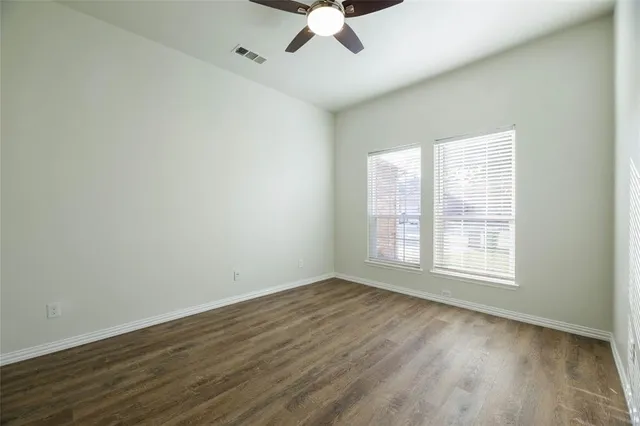 an empty room with wooden floor chandelier fan and windows