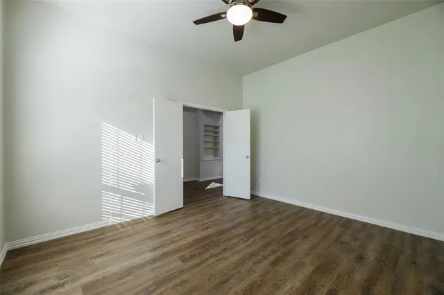 an empty room with wooden floor chandelier fan and windows