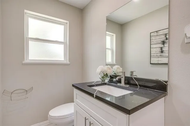 a bathroom with a granite countertop sink a toilet and a window