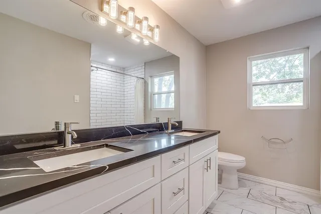 a bathroom with a granite countertop sink a toilet a mirror and a window