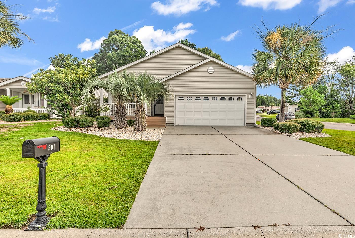 Ranch-style house featuring an attached garage, concrete driveway, covered porch, and a front yard