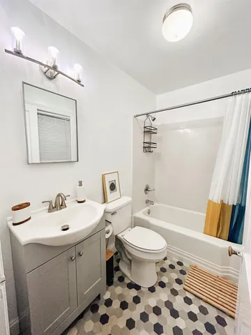 a bathroom with a sink a toilet a mirror a lamp a bathtub and vanity