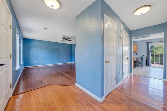 a view of a hallway to an empty room with wooden floor and a window