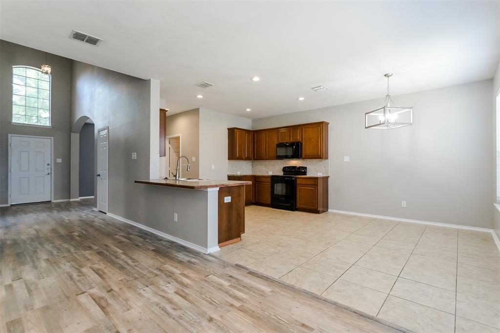 203 Arabian Road Waxahachie, TX 75165 - Photo 2 of 24 Open-concept living area featuring wood-finish flooring, a kitchen with dark wood cabinetry and black appliances, a breakfast bar, and an overhead lighting fixture