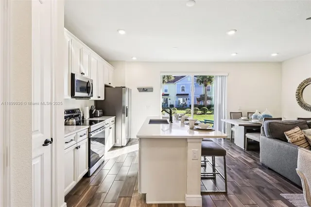 a living room with stainless steel appliances furniture a flat screen tv and a kitchen