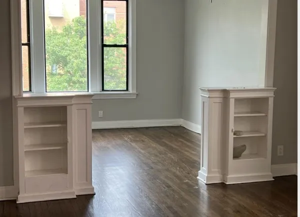 an empty room with wooden floor cabinet and window