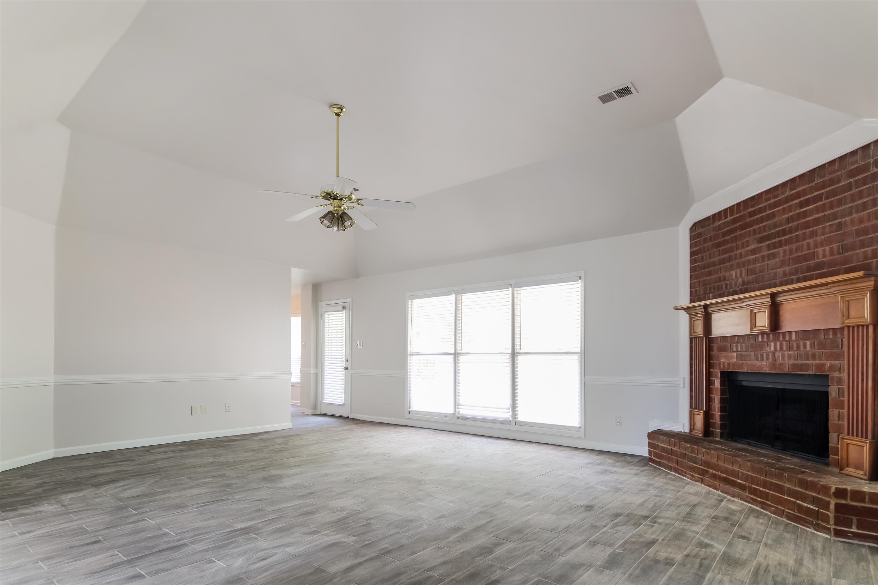 8859 Raspberry Lane Memphis, TN 38016 - Photo 4 of 16 Unfurnished living room featuring ceiling fan, brick wall, vaulted ceiling, light hardwood / wood-style flooring, and a brick fireplace