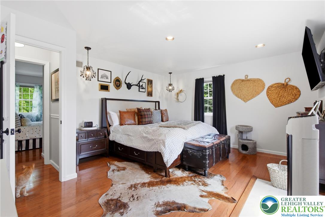 890 Lahr Road Nazareth, PA 18064 - Photo 27 of 71 Hardwood flooring flows through this inviting primary bedroom, highlighted by sparkling chandelier lighting.