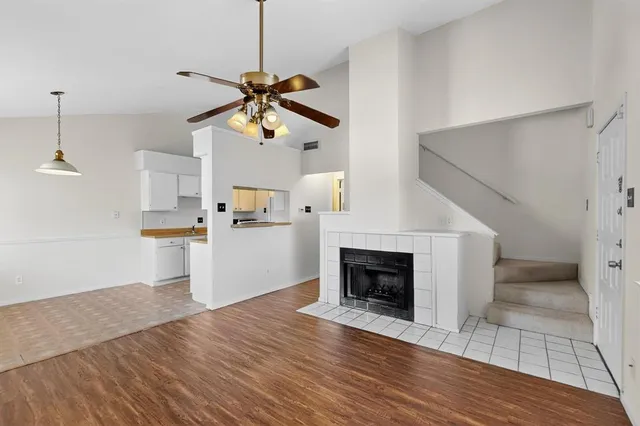 a view of a room with wooden floor a ceiling fan and kitchen view
