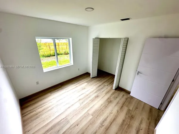 a view of an empty room with wooden floor and a window