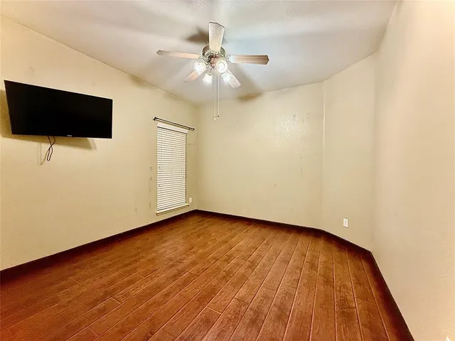 a view of an empty room with wooden floor and a ceiling fan