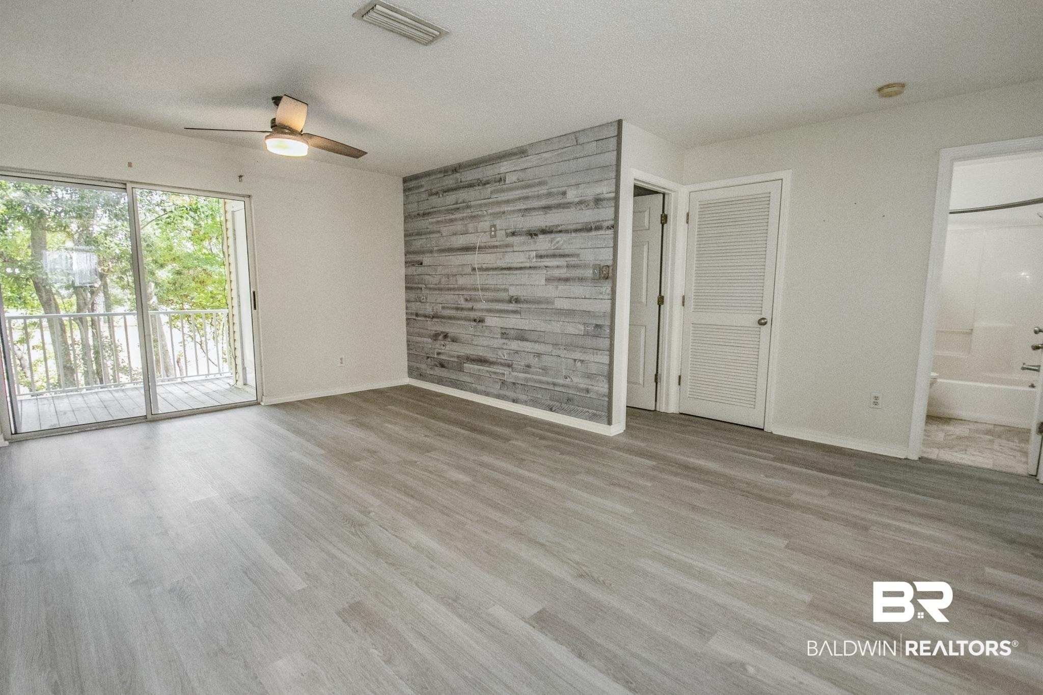 25957 Canal Road, Unit 203 Orange Beach, AL 36561 - Photo 8 of 28 Unfurnished living room with wooden walls, light wood-style floors, ceiling fan, a textured ceiling, and an accent wall