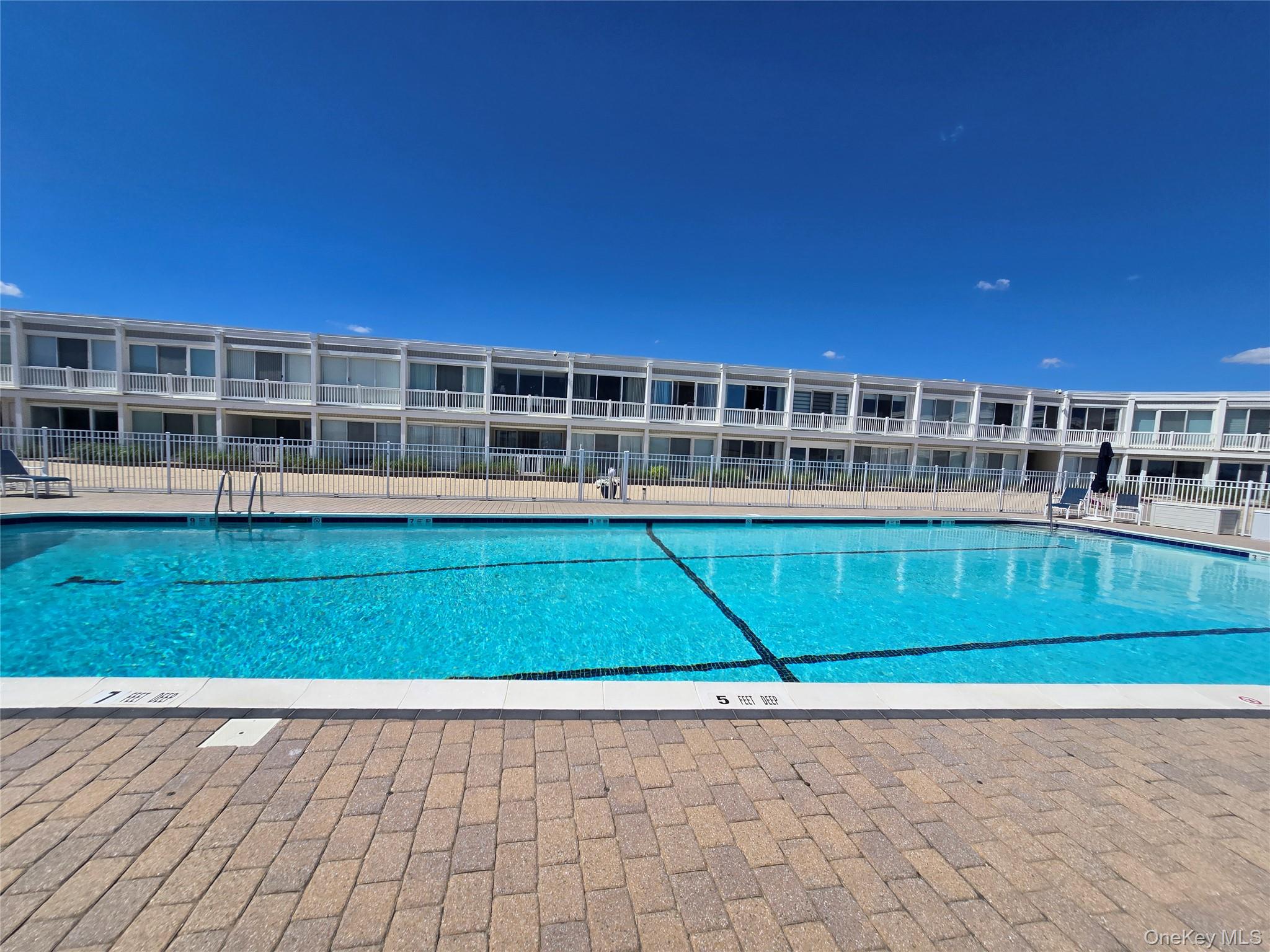 585 Dune Road, Unit L10 Westhampton, NY 11978 - Photo 4 of 25 Community swimming pool featuring a perimeter fence and a surrounding paver patio