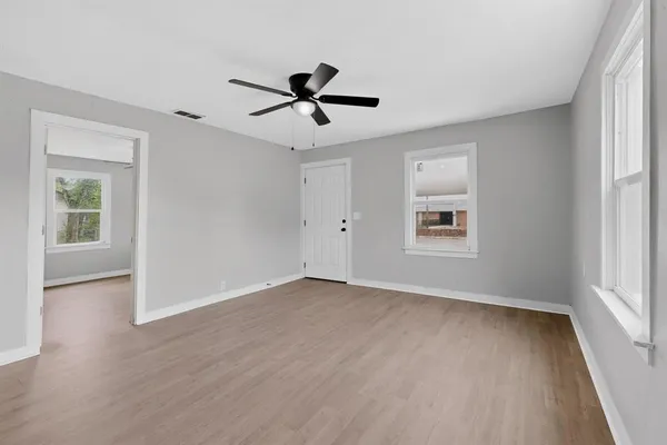 an empty room with wooden floor ceiling fan and windows