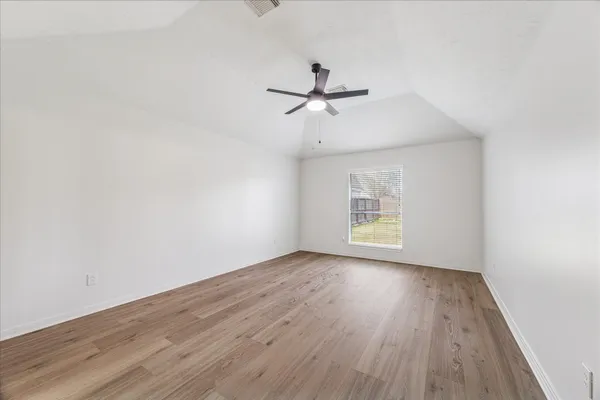an empty room with wooden floor ceiling fan and windows