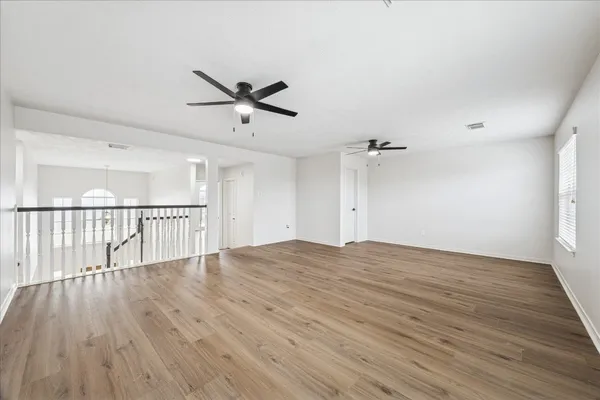 an empty room with wooden floor fan and windows