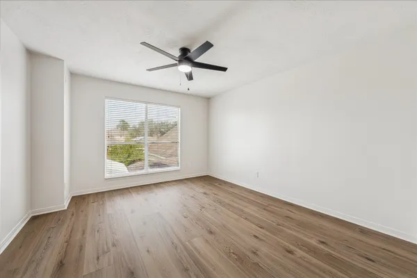 an empty room with wooden floor fan and windows