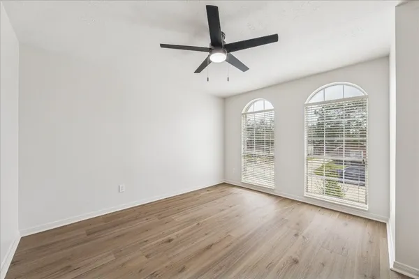 an empty room with wooden floor fan and windows
