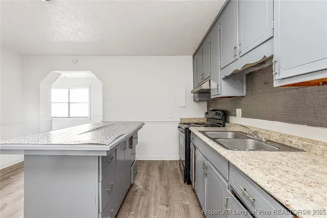 a kitchen with granite countertop stainless steel appliances a sink a stove and a wooden floors