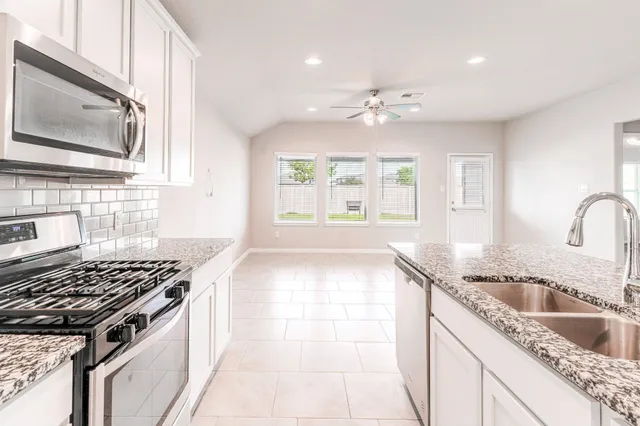 a kitchen with granite countertop a sink a stove cabinets and stainless steel appliances
