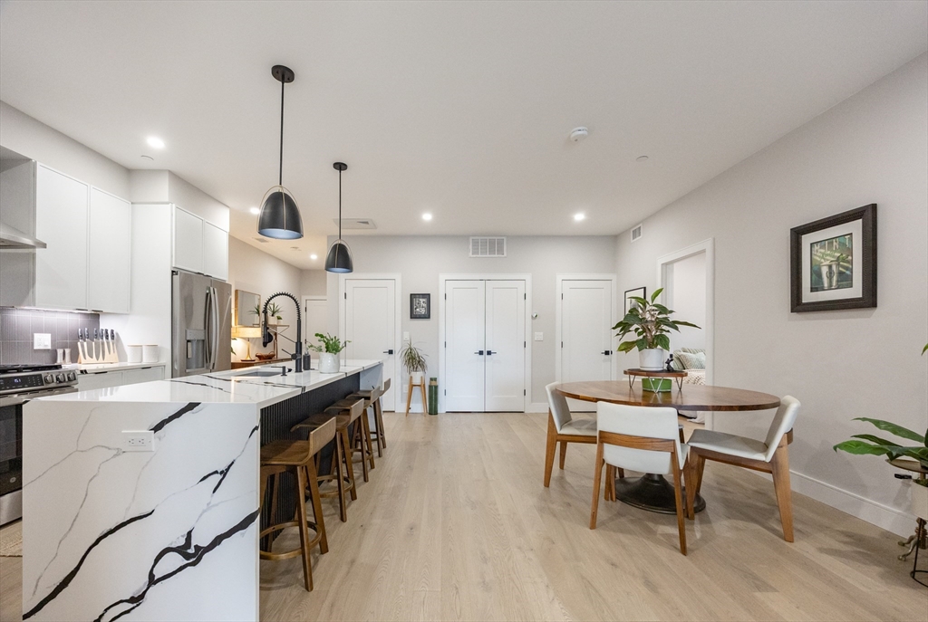 70 Shawsheen Road, Unit PH5 Boston, MA 02128 - Photo 14 of 42 a kitchen with stainless steel appliances kitchen island granite countertop a stove a sink a dining table and chairs with wooden floor
