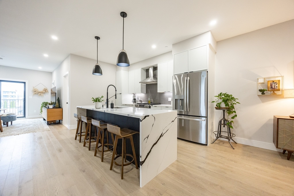 70 Shawsheen Road, Unit PH5 Boston, MA 02128 - Photo 3 of 42 a kitchen with kitchen island a refrigerator a stove a sink a dining table and chairs with wooden floor