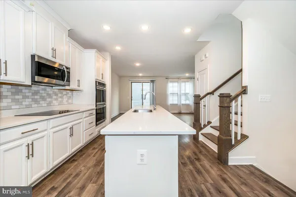 a kitchen with stainless steel appliances granite countertop a sink a microwave a refrigerator and white cabinets with wooden floor