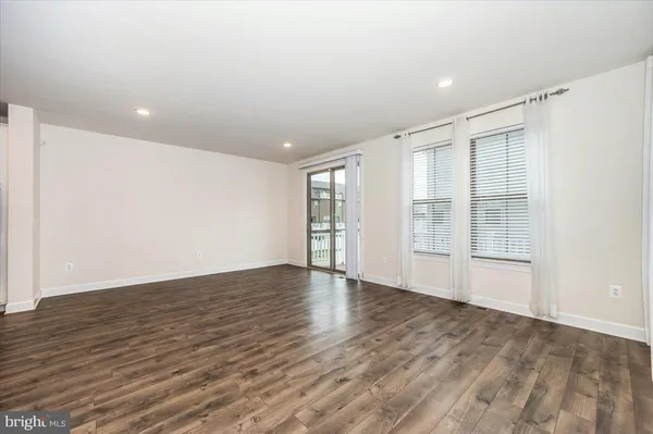 a view of an empty room with wooden floor and a kitchen