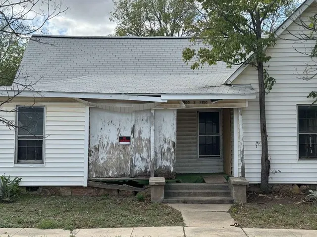a view of a small house with potted plants and large tree