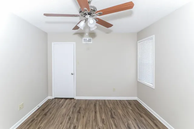 an empty room with wooden floor fan and windows