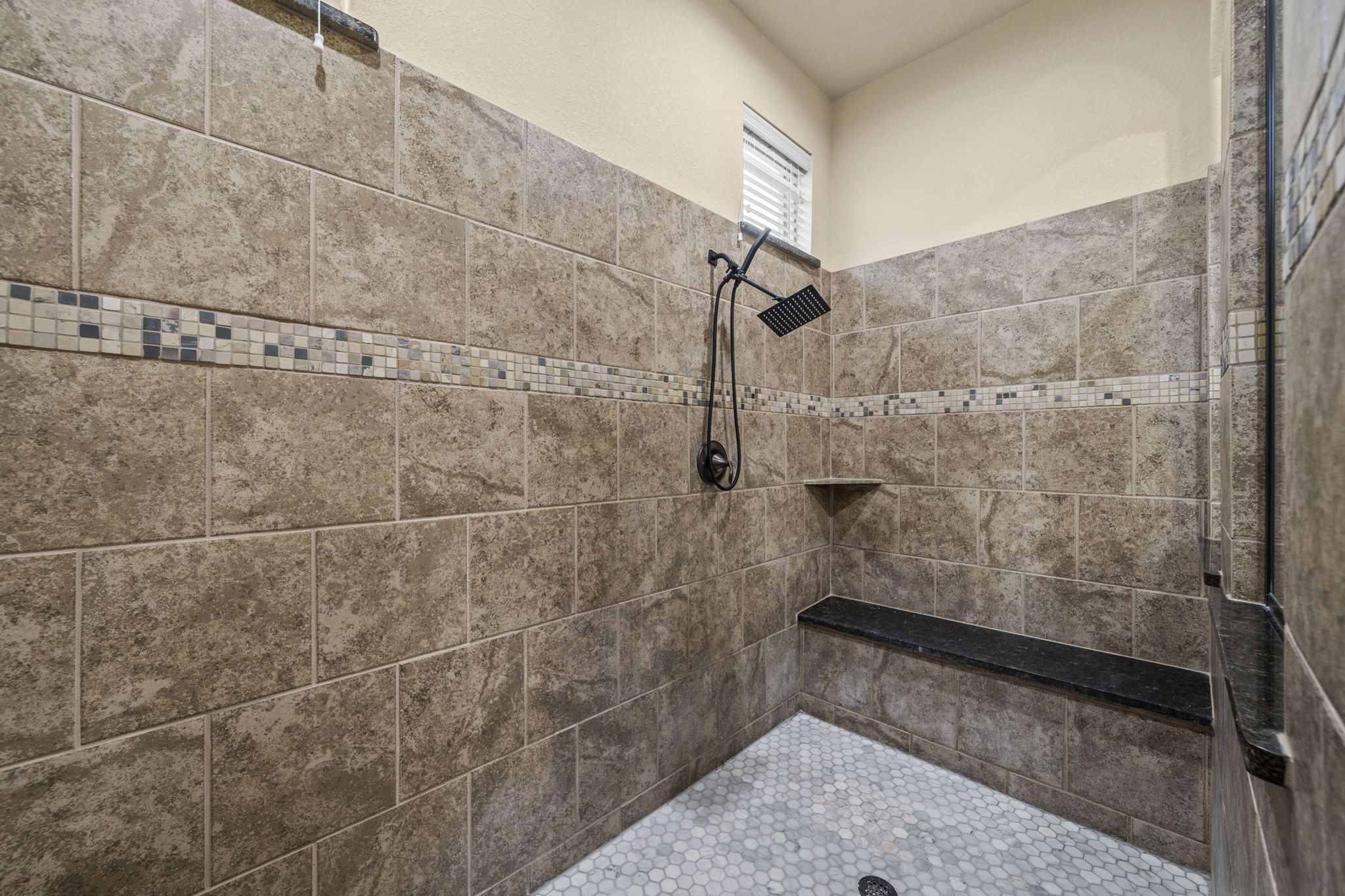 14215 Spindle Arbor Road Cypress, TX 77429 - Photo 32 of 47 This spacious shower features elegant brown tile with a decorative mosaic accent strip, a sleek rainfall showerhead, built-in bench, and a small window for natural light.