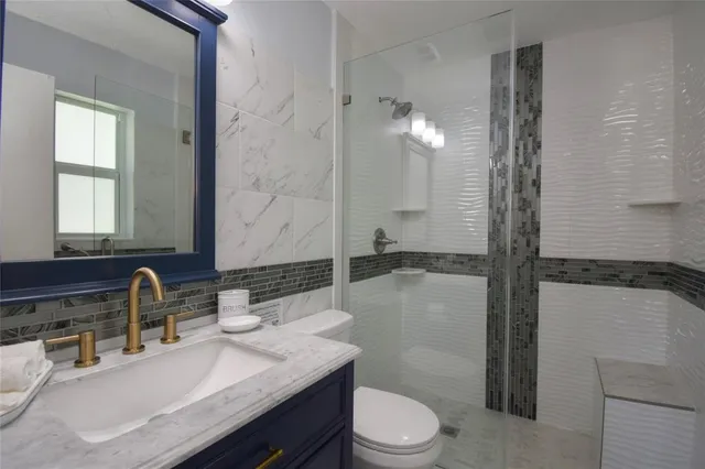 a bathroom with a granite countertop sink a toilet a mirror and shower