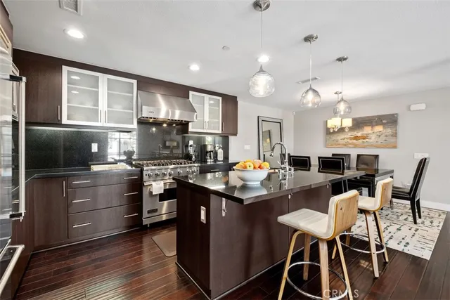 a kitchen with stainless steel appliances granite countertop a stove top oven a sink dishwasher a dining table and chairs with wooden floor