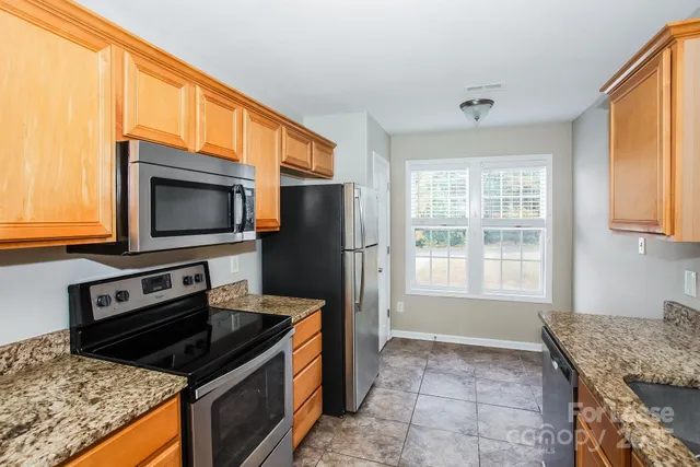 a kitchen with granite countertop a stove top oven microwave and refrigerator