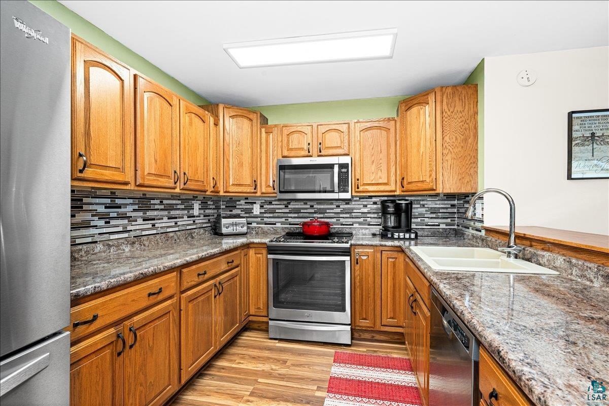 130 West Austin Street Duluth, MN 55803 - Photo 7 of 35 Full kitchen featuring wood cabinetry, stainless steel appliances, speckled countertops, and a mosaic tile backsplash