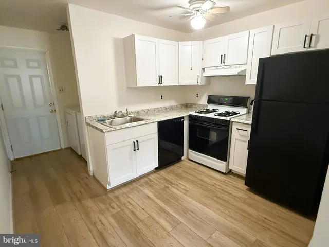 a kitchen with stainless steel appliances granite countertop a stove top oven a refrigerator a white cabinets and wooden floor