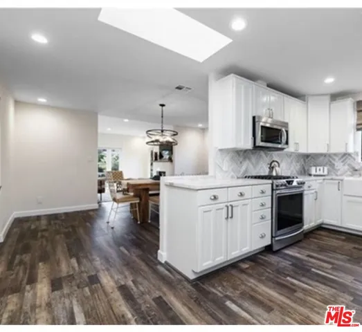 a kitchen with granite countertop a stove top oven a sink dishwasher and white cabinets with wooden floor