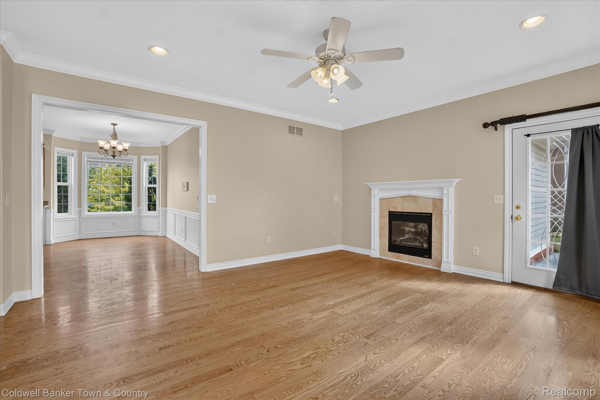 1725 Town Commons Drive Howell, MI 48855 - Photo 27 of 53 Spacious living area featuring wood-finish flooring, a fireplace with a decorative mantel and stone surround, and an illuminated ceiling fan