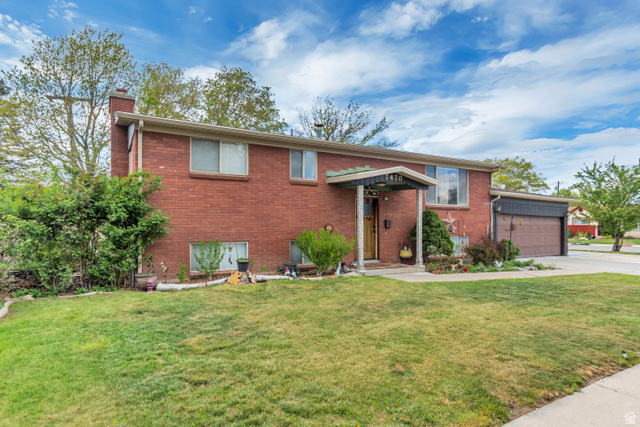 7470 Ramanee Drive Midvale, UT 84047 - Photo 1 of 29 Split foyer home featuring a front yard, a chimney, brick siding, concrete driveway, and an attached garage