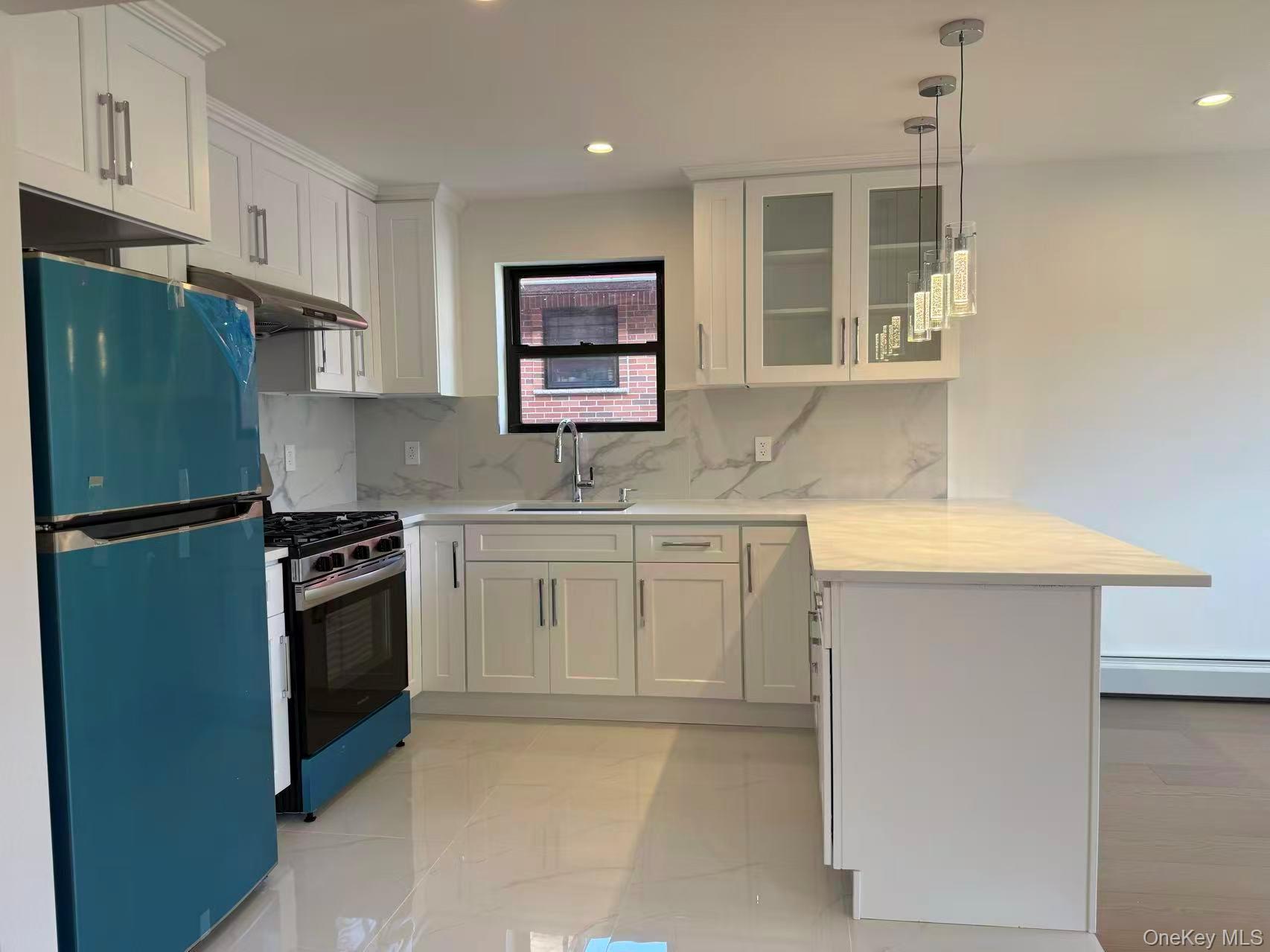 43-44 161 Street Queens, NY 11358 - Photo 3 of 12 Kitchen featuring a peninsula, freestanding refrigerator, glass insert cabinets, white cabinets, and gas stove