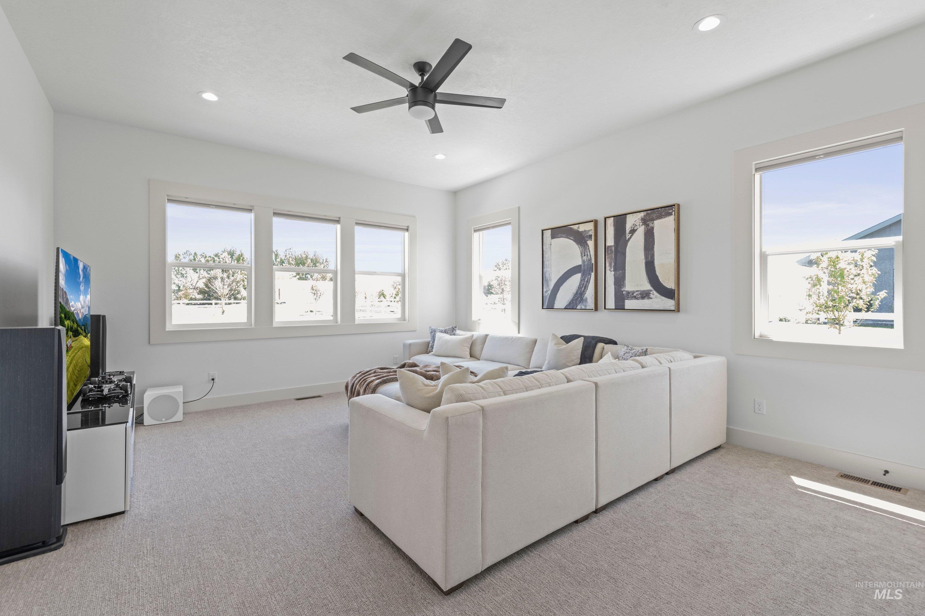 24990 Belgian Way Middleton, ID 83644 - Photo 33 of 50 Spacious room featuring light gray carpeting, multiple large windows with white trim, a dark-toned ceiling fan, and recessed lighting