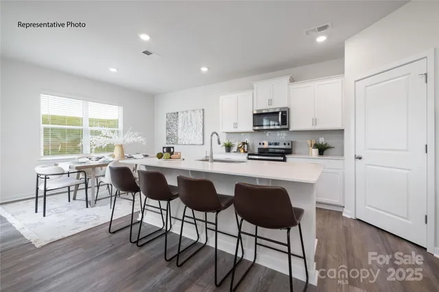 a kitchen with stainless steel appliances granite countertop a stove a sink a microwave a refrigerator a dining table and chairs with wooden floor