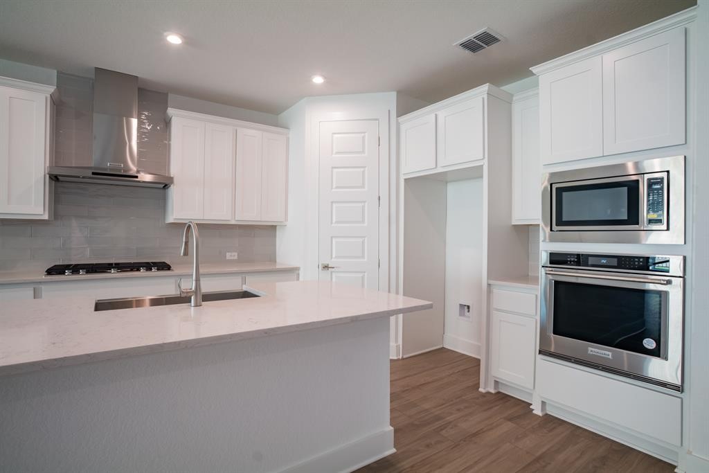 4612 Modena Bay Bend Leander, TX 78641 - Photo 14 of 34 Kitchen with stainless steel appliances, wall chimney exhaust hood, white cabinetry, decorative backsplash, and dark wood-style floors