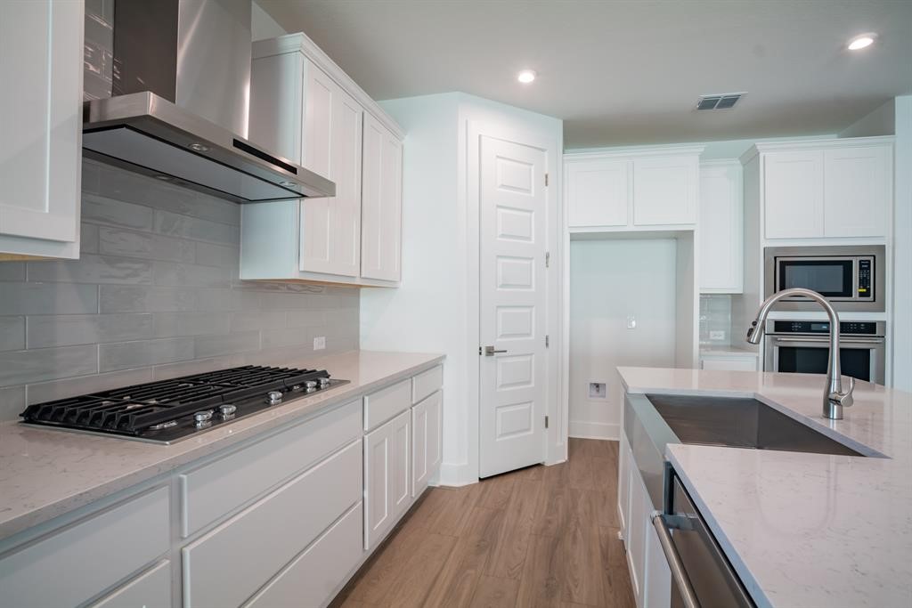 4612 Modena Bay Bend Leander, TX 78641 - Photo 19 of 34 Kitchen with wall chimney exhaust hood, white cabinetry, light stone counters, light wood-style floors, and recessed lighting