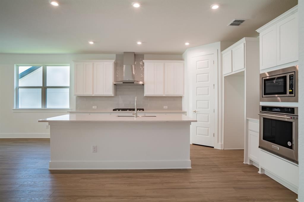 4612 Modena Bay Bend Leander, TX 78641 - Photo 9 of 34 Kitchen featuring stainless steel appliances, wall chimney range hood, white cabinetry, light wood-type flooring, and recessed lighting