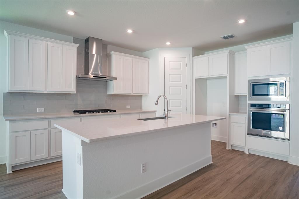 4612 Modena Bay Bend Leander, TX 78641 - Photo 10 of 34 Kitchen featuring stainless steel appliances, white cabinets, wall chimney exhaust hood, tasteful backsplash, and a kitchen island with sink